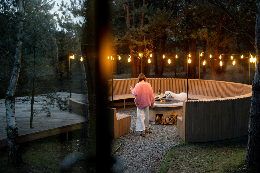 A person enjoys a serene outdoor audio setup in a wood-paneled fire pit area with string lights at dusk in Birmingham.