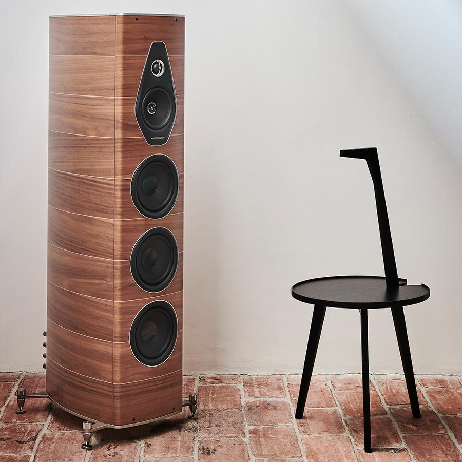 Curved wood floorstanding speaker beside a simple black chair