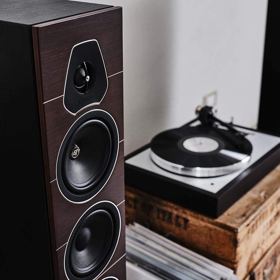 Slim speaker next to a turntable and stacked vinyl records