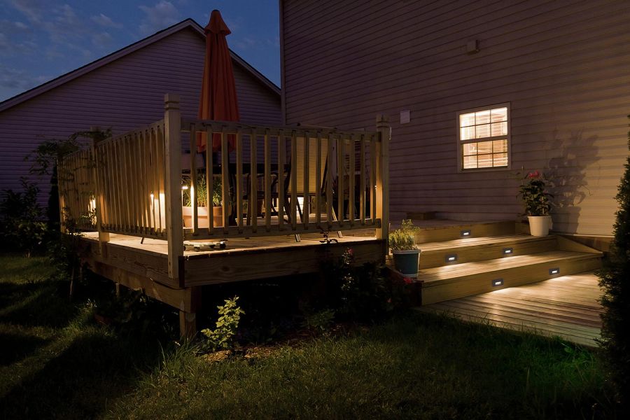 Backyard wooden deck and steps lit with warm deck lighting at night
